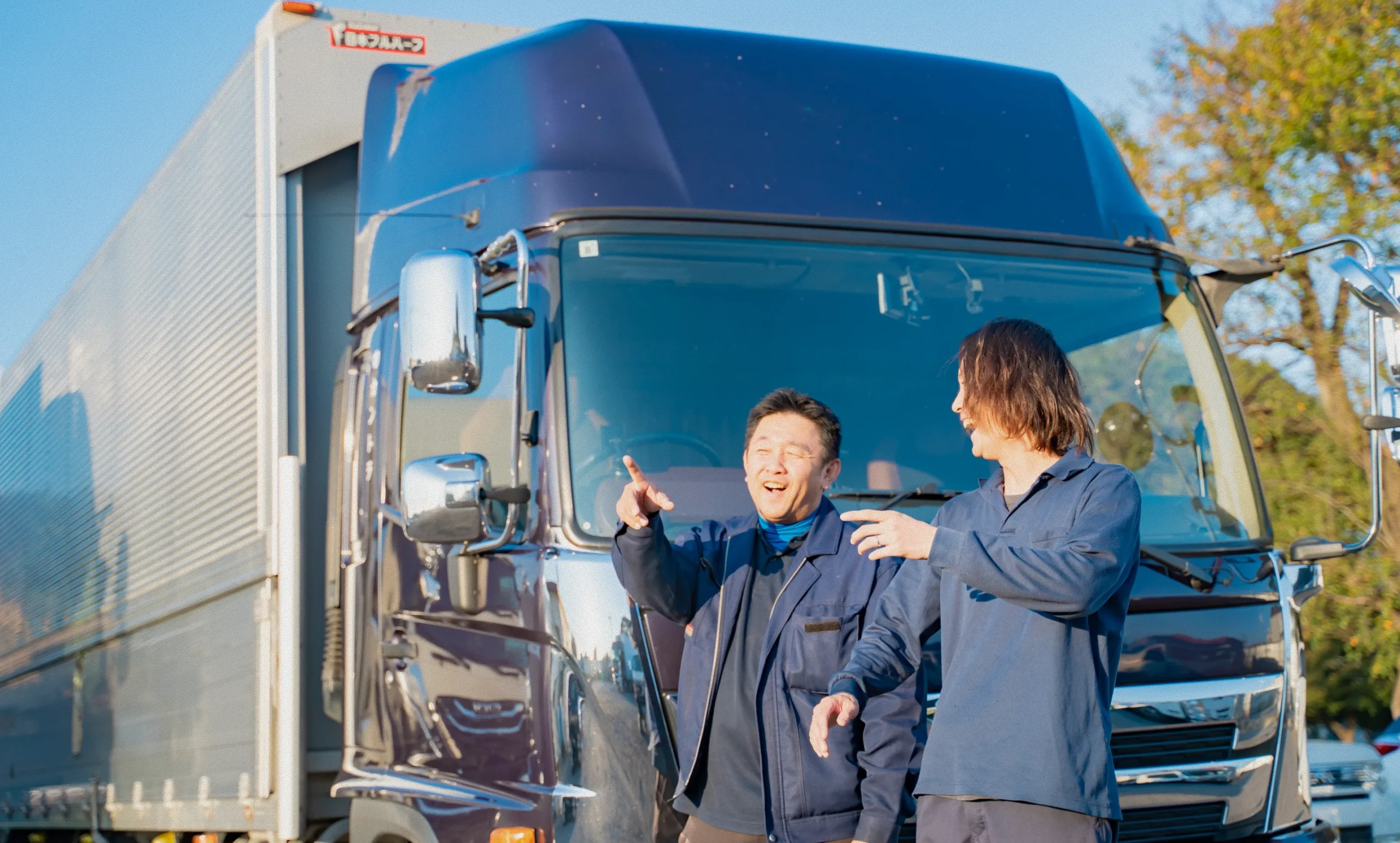 大型トラックの前で笑顔で話す作業服姿の二人の男性