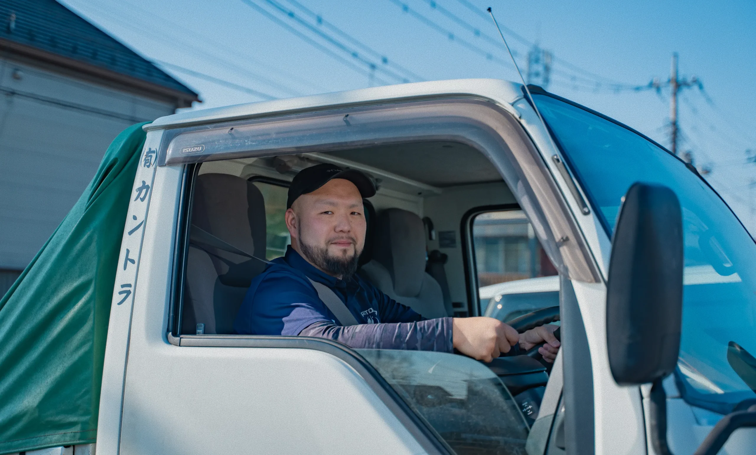 トラックの運転席で笑顔を見せるキャップをかぶった男性運転手