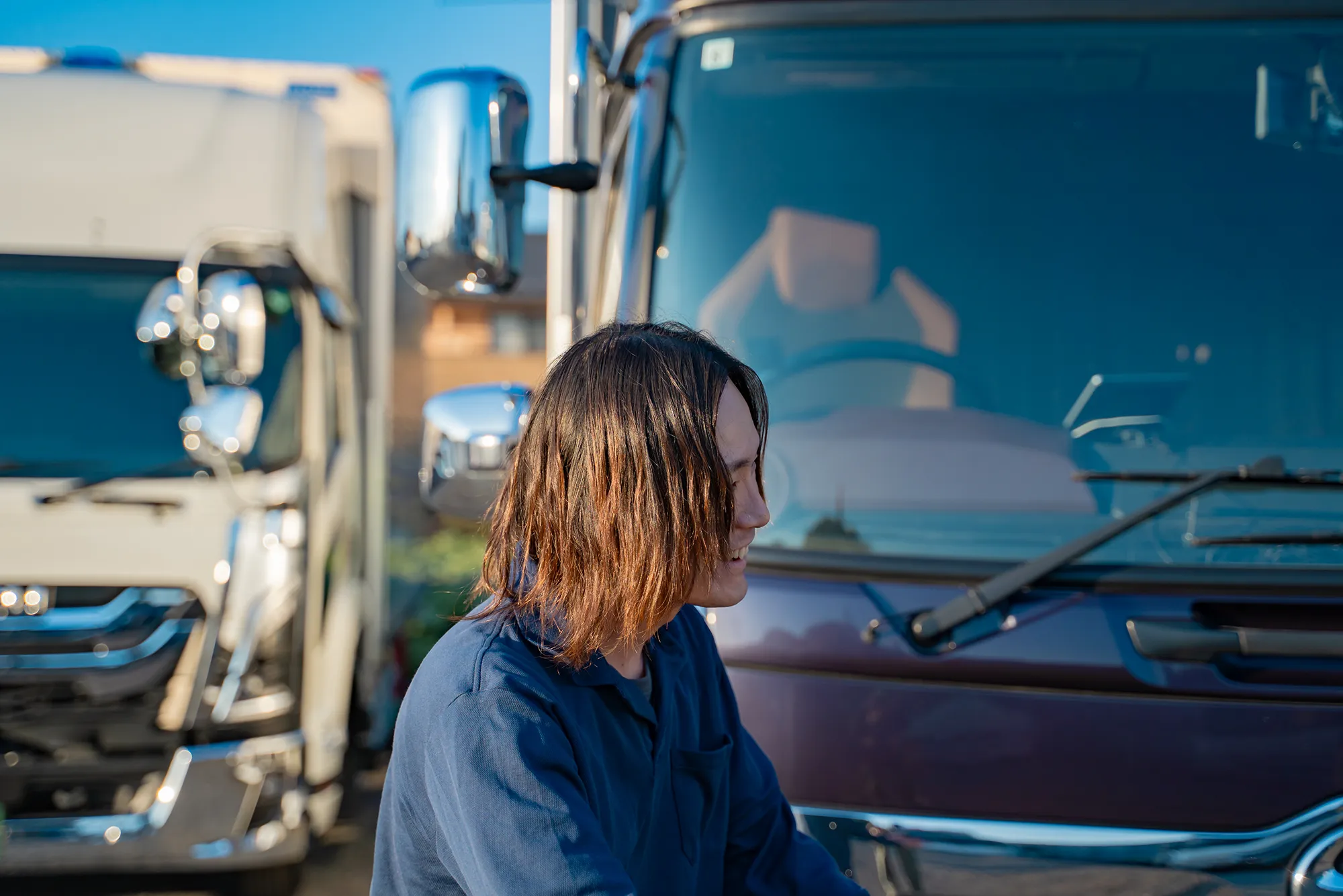 トラック前で横向きに微笑む作業服の人物姿