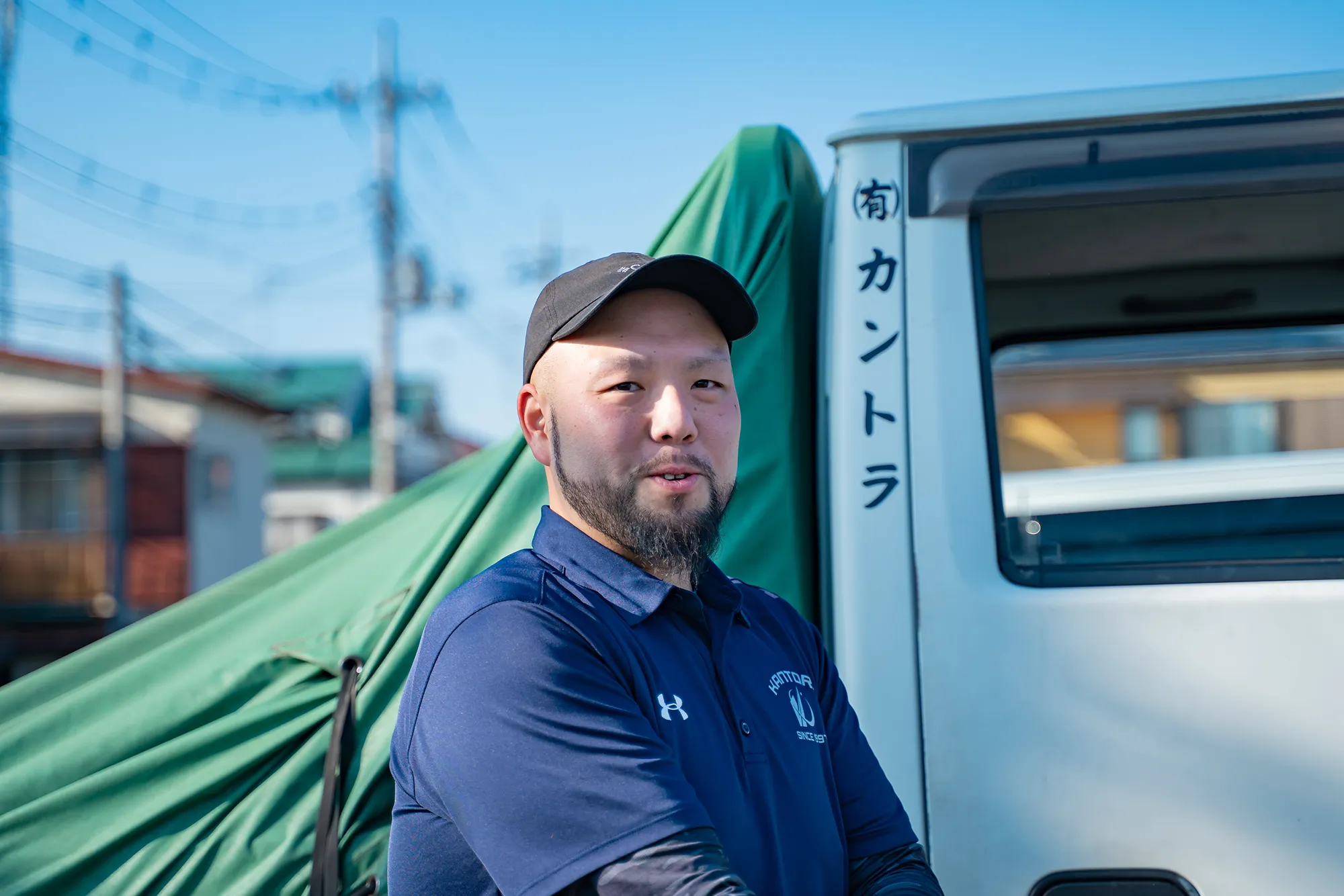 荷台横で腕を組み微笑む作業服のドライバー