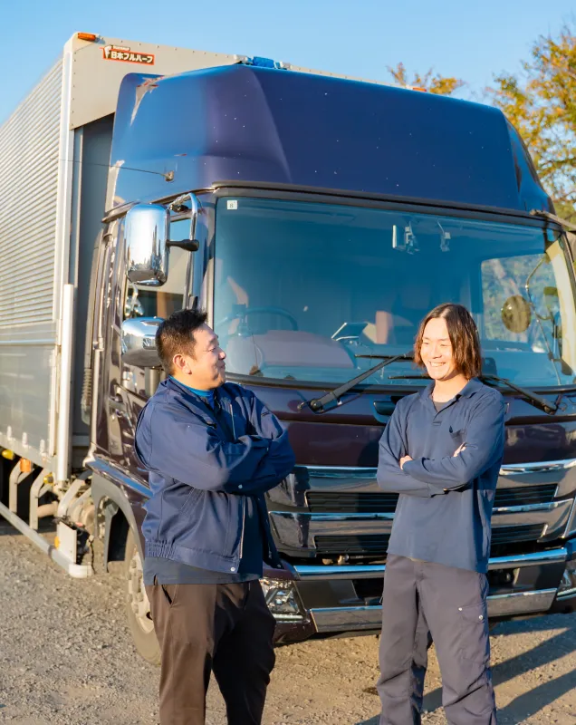 大型トラック前で向かい合い話す二人の作業者