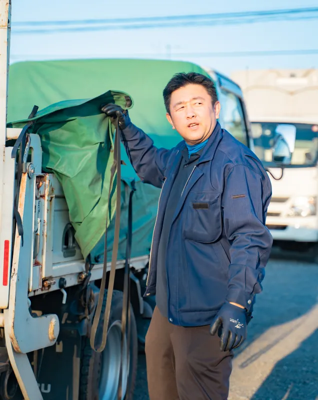 荷台のシートを引き上げる作業者の横姿