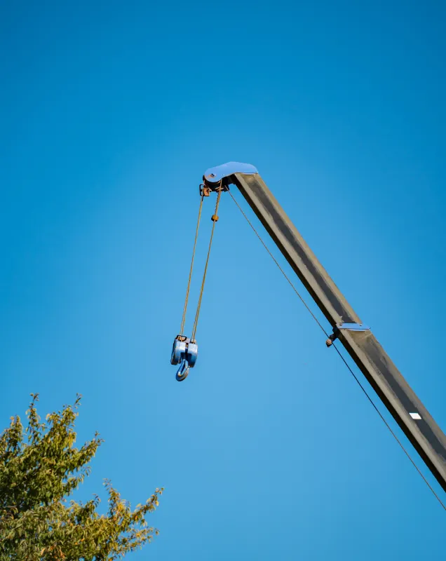 青空に伸びるクレーン先端と吊りフック