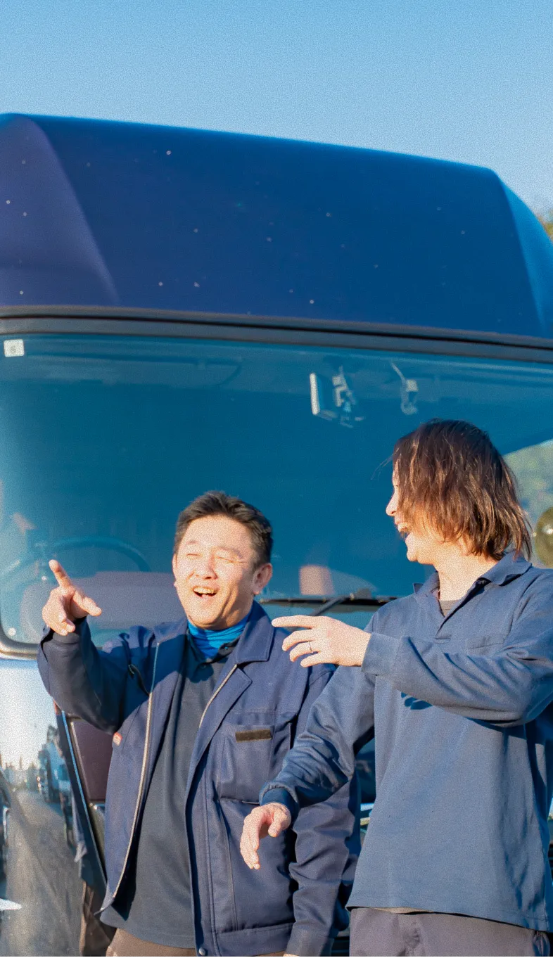 大型トラックの前で笑顔で話す作業服姿の二人の男性