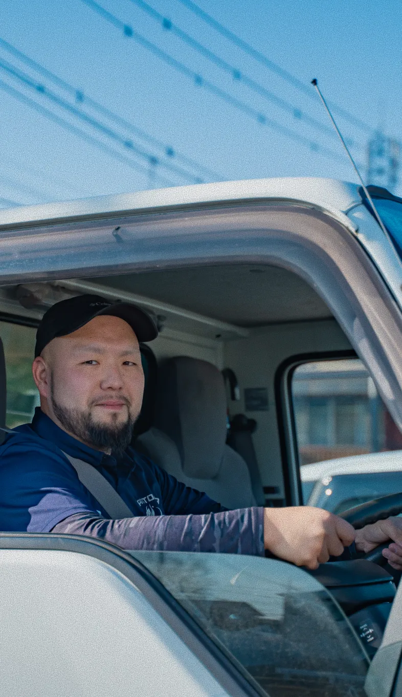 トラックの運転席で笑顔を見せるキャップをかぶった男性運転手