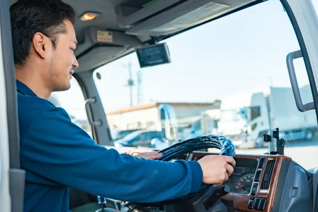 トラックの運転席で笑顔を見せる作業服の男性運転手
